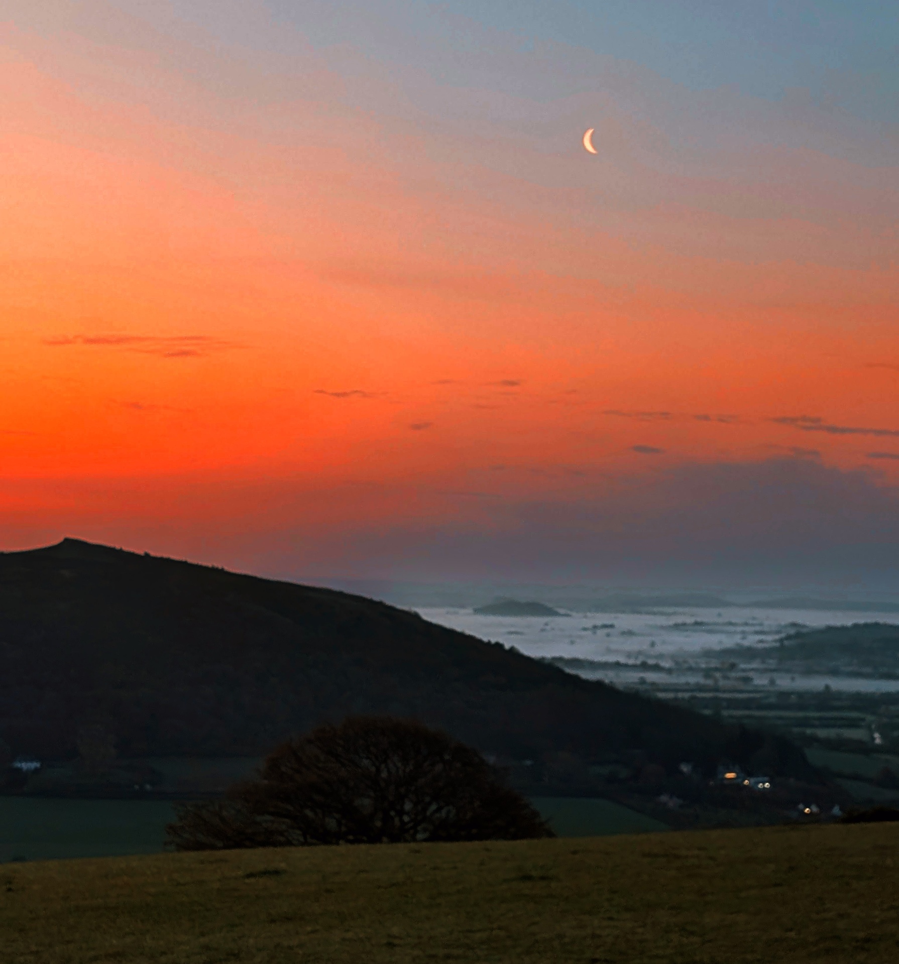 Crescent moon over a red dawn sky above the Somerset Levels